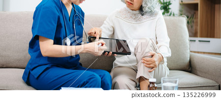 Asian Nurse Using Tablet to Review Bone X-ray Results with Elderly Woman at Home, Home Healthcare Concept 135226999