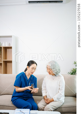 Young nurse holding a bottle of pills and discussing treatment with an elderly Asian woman during a medical consultation Young nurse holding a bottle of pills and discussing treatment with an elderly Asian woman during a medical consultation 135227038