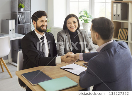 Real-estate agent or financial advisor shaking hands with couple during meeting in office 135227232