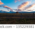 Scenic landscape features wooden fence, farm house, and dramatic sunset clouds over a rural area in the evening 135229381