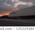 Large truck moving quickly along a highway during a vibrant sunset with dramatic clouds in the background 135229384