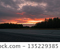 Sunset over a rural road surrounded by trees at dusk creating a serene atmosphere 135229385