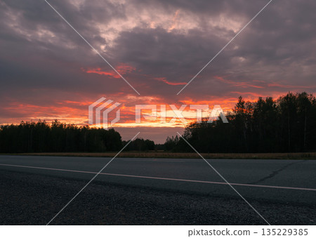 Sunset over a rural road surrounded by trees at dusk creating a serene atmosphere Sunset over a rural road surrounded by trees at dusk creating a serene atmosphere 135229385