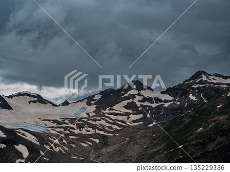 Mountain range partially covered by clouds and snow near a glacier on an overcast day in Caucasus Mountain range partially covered by clouds and snow near a glacier on an overcast day in Caucasus 135229386