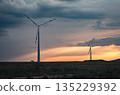 Wind turbines silhouetted against a vibrant sunset over rolling fields in rural landscape 135229392