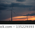 Wind turbines silhouetted against a vibrant sunset over rolling fields in rural landscape 135229393