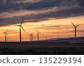 Wind turbines silhouetted against a vibrant sunset over rolling fields in rural landscape 135229394