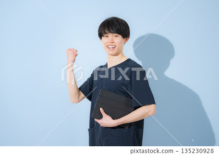 Image of a young male nurse or doctor wearing a scrub against a light blue background Image of a young male nurse or doctor wearing a scrub against a light blue background 135230928