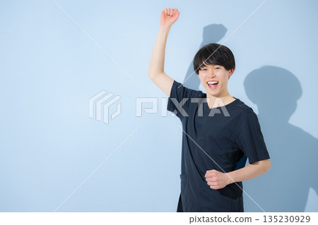 一張年輕男護士或醫生身穿手術服，站在淺藍色背景前，握拳的照片 135230929