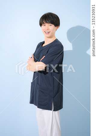 一位年輕的男護士或醫生身穿手術服,站在淺藍色背景前,面帶微笑,雙手交叉看著鏡頭。 一位年輕的男護士或醫生身穿手術服,站在淺藍色背景前,面帶微笑,雙手交叉看著鏡頭。 135230931