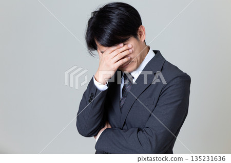 A middle-aged male businessman in a suit who is worried and covering his face A middle-aged male businessman in a suit who is worried and covering his face 135231636