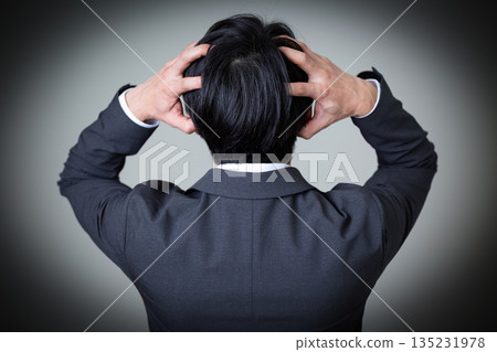 一位身穿西裝的中年男商人抱著頭,神情憂慮。 一位身穿西裝的中年男商人抱著頭,神情憂慮。 135231978