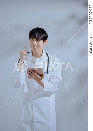 A young male doctor in a white coat holding a tablet A young male doctor in a white coat holding a tablet 135232052