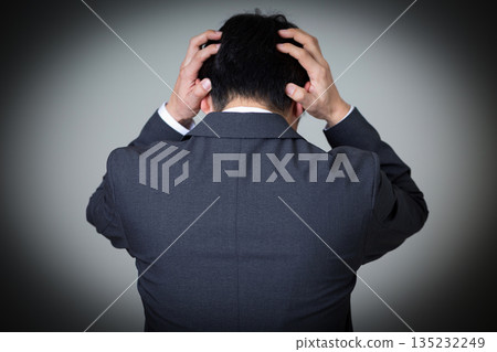 一位身穿西裝的中年男商人抱著頭,神情憂慮。 一位身穿西裝的中年男商人抱著頭,神情憂慮。 135232249