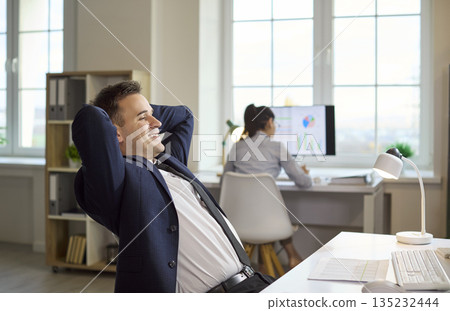 Happy businessman relaxing at desk after success, office victory and achievement 135232444