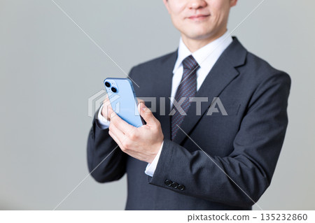 A middle-aged male businessman in a suit operating a smartphone A middle-aged male businessman in a suit operating a smartphone 135232860