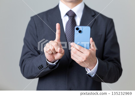 A middle-aged male businessman in a suit holding a smartphone and pointing his index finger 135232969