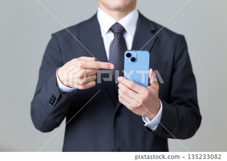 A middle-aged male businessman in a suit pointing at his smartphone 135233082