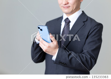 A middle-aged male businessman in a suit operating a smartphone 135233363