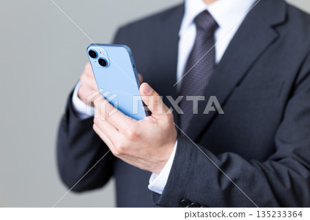 A middle-aged male businessman in a suit operating a smartphone 135233364