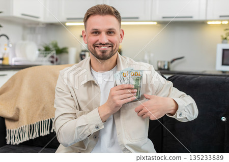 Young man counts cash dollars smiles happy with savings plans dream purchase investment bonus salary 135233889