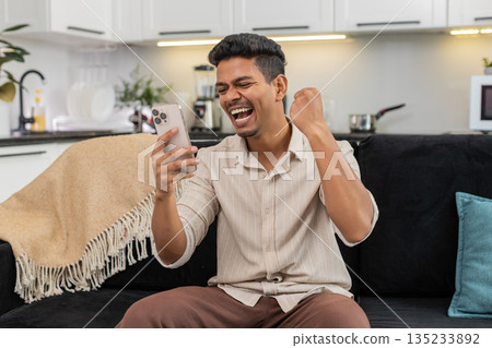Indian man reads message on smartphone smiles makes victory gesture big thumbs up celebrates triumph Indian man reads message on smartphone smiles makes victory gesture big thumbs up celebrates triumph 135233892