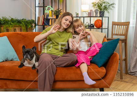 Mother daughter dog video call on smartphone wave hello heart gesture warm family chat with grandma Mother daughter dog video call on smartphone wave hello heart gesture warm family chat with grandma 135233896