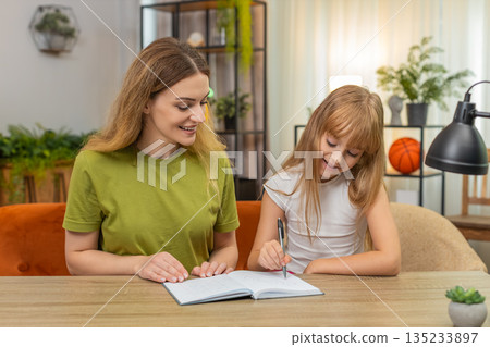 Mother daughter play tic tac toe on paper rounds keep score notebook laugh rematch at table together 135233897