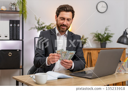 Middle-aged businessman counts cash dollars records budget on laptop writes notes in notebook plans Middle-aged businessman counts cash dollars records budget on laptop writes notes in notebook plans 135233918