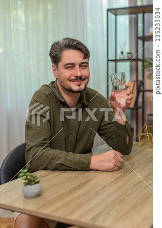 Middle-aged man drinks water glass practicing healthy habit hydration wellness routine at table desk Middle-aged man drinks water glass practicing healthy habit hydration wellness routine at table desk 135233934