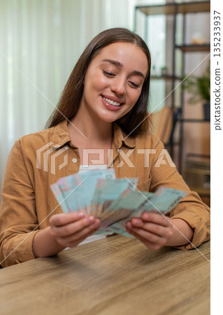 Young woman counting money hryvnia cash satisfied with salary earnings celebrating financial success Young woman counting money hryvnia cash satisfied with salary earnings celebrating financial success 135233937