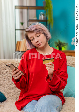 Young woman making online shopping purchase using smartphone credit card satisfied joyful expression Young woman making online shopping purchase using smartphone credit card satisfied joyful expression 135233942