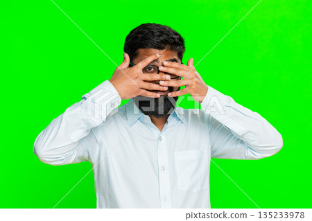 Indian man covering one eye with hand in spy gesture showing intrigue mystery secret peek chroma key 135233978