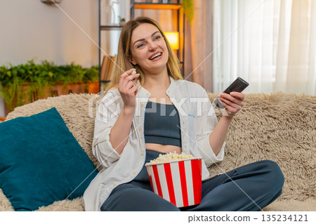 Adult woman laughing while watching comedy on television at home, joyful expression and relaxed mood Adult woman laughing while watching comedy on television at home, joyful expression and relaxed mood 135234121