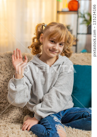 Young teenager girl waving hand with cheerful expression saying hello or goodbye indoors at home 135234166