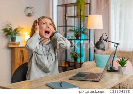 Frustrated freelancer using laptop struggling to work due to loud noise sitting at home office table 135234188