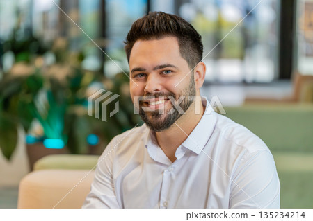 Portrait of smiling young businessman looking at camera sitting in hotel lobby Portrait of smiling young businessman looking at camera sitting in hotel lobby 135234214