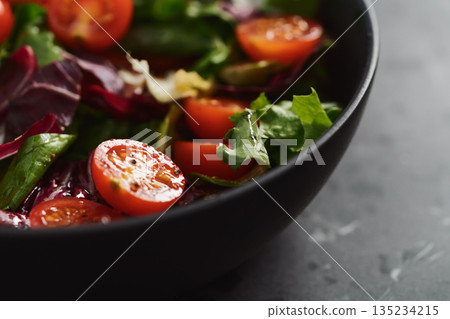 Salad with green and purple leaves and cherry tomatoes in black bowl 135234215