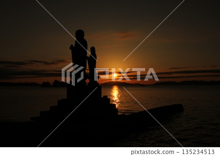 The silhouette of a Buddha statue in the sunset and the calm Lake Shinji 135234513