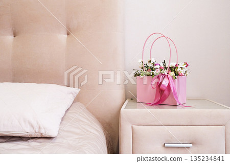 Pink flowers in gift bag on bedside table in bedroom. Pink flowers in gift bag on bedside table in bedroom. 135234841