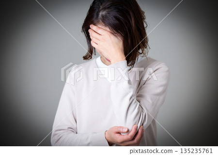 A middle-aged woman suffering while covering her face A middle-aged woman suffering while covering her face 135235761