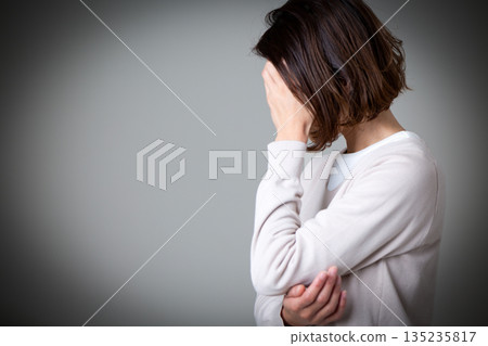 一位中年婦女摀著臉，痛苦不堪。 135235817