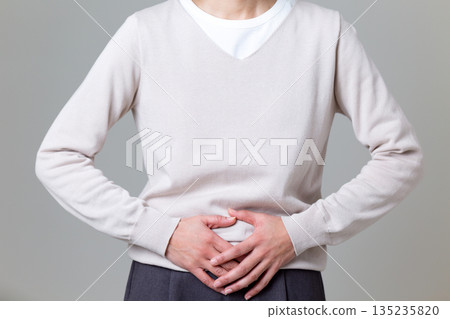Middle-aged woman suffering from abdominal pain while holding her lower abdomen Middle-aged woman suffering from abdominal pain while holding her lower abdomen 135235820