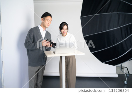 在攝影棚裡，男男女女正在電腦上查看照片。 135236804