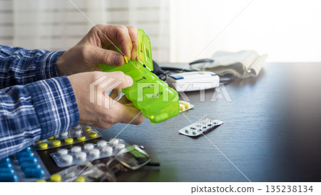 Middle aged caucasian man distributing scheduled dose of medication in dosette box 135238134