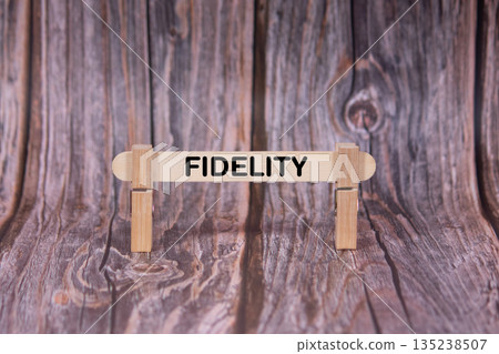 Fidelity symbol. A wooden stick clasped by clothespins set over a beautiful Brown Grunge Wooden Texture Background. Business and Fidelity concept with copy space Fidelity symbol. A wooden stick clasped by clothespins set over a beautiful Brown Grunge Wooden Texture Background. Business and Fidelity concept with copy space 135238507