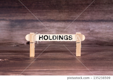 Holdings symbol. Clothespins gripping a wooden stick against a beautiful Brown Wooden Background . Business and Holdings concept with copy space 135238509