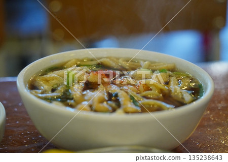 Delicious Korean style udon noodle soup with green vegetables in a white bowl, close up shot Delicious Korean style udon noodle soup with green vegetables in a white bowl, close up shot 135238643