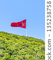 A large Turkish flag flies at the top of the hill, surrounded by bright green foliage and clear skies. 135238758