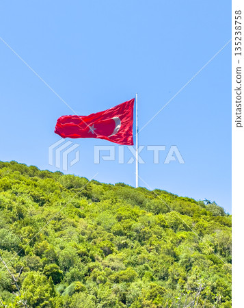 A large Turkish flag flies at the top of the hill, surrounded by bright green foliage and clear skies. 135238758